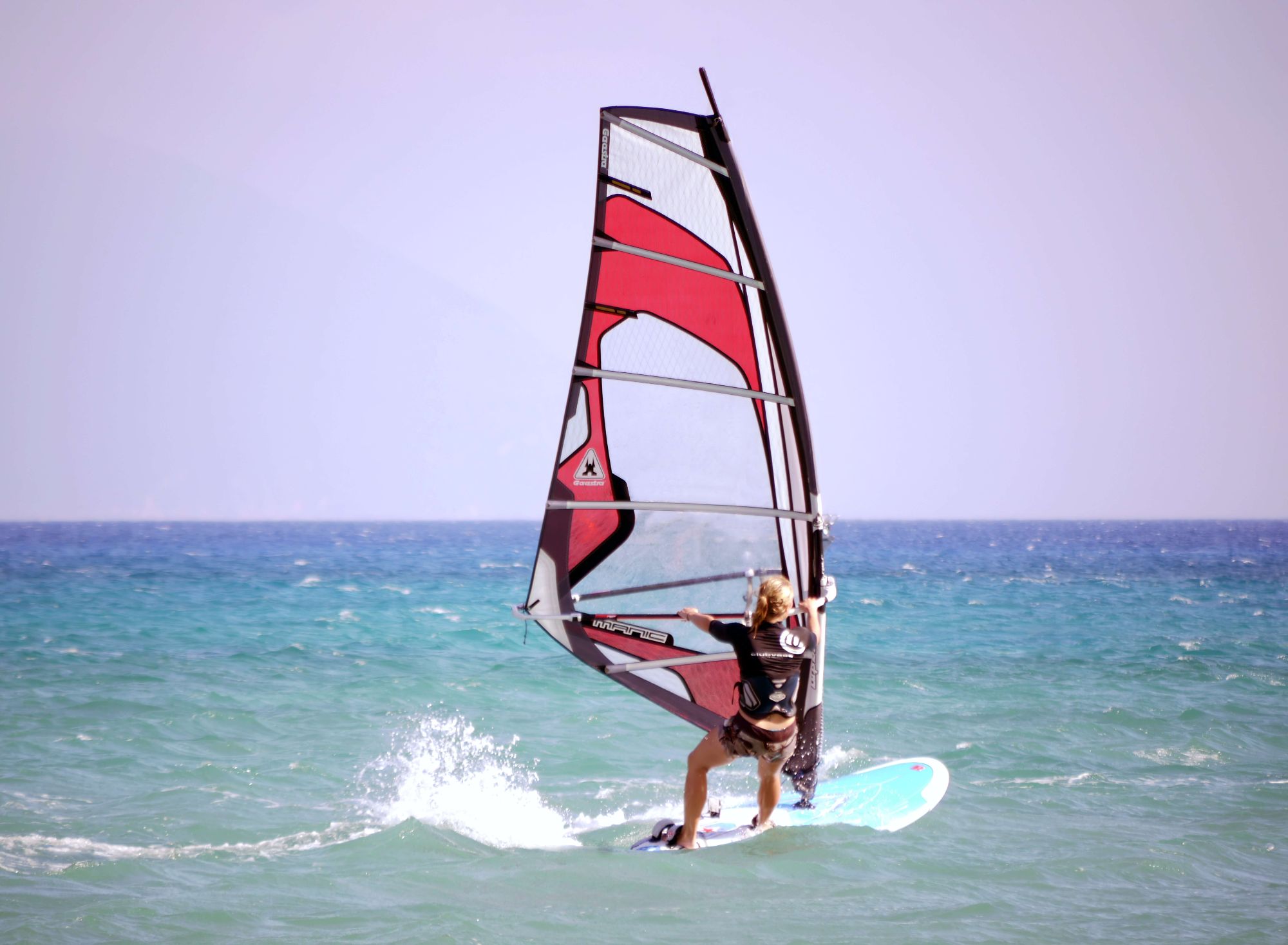 Lady is windsurfing around a yacht