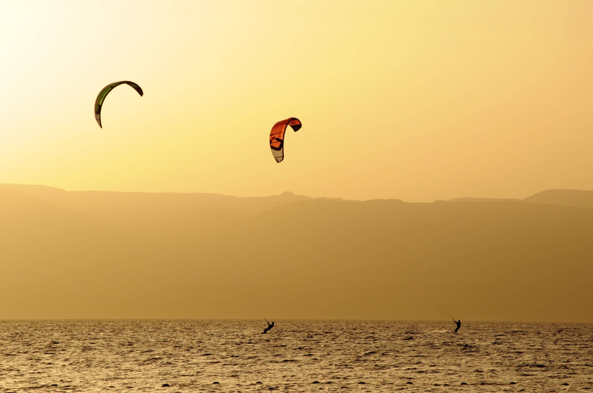 Two people are kitesurfing in the sunset